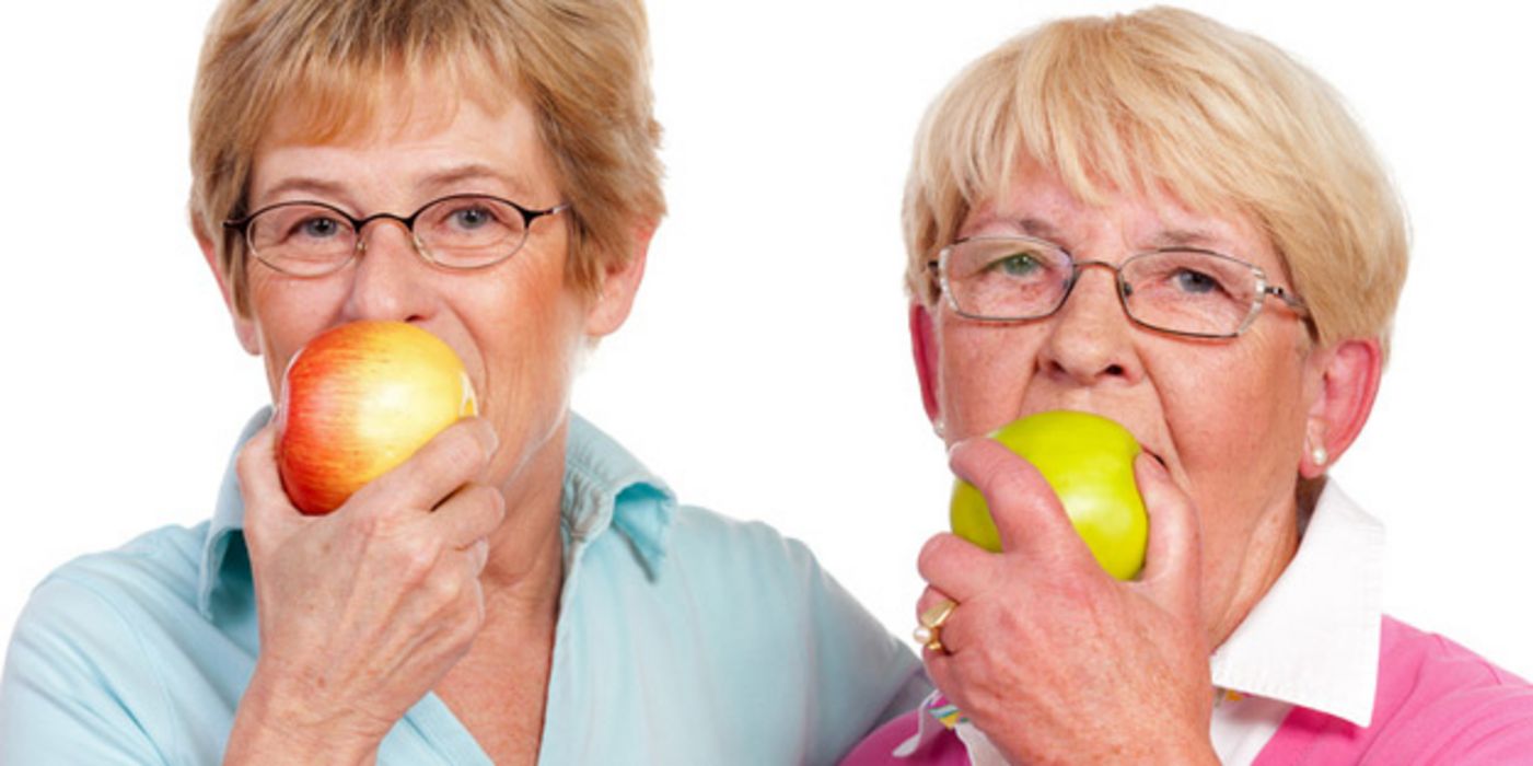 Zwei Seniorinnen beißen in Äpfel