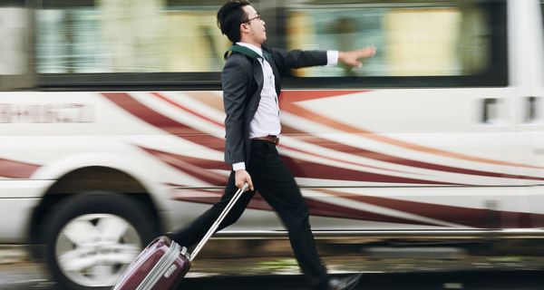 Junger Mann in Arbeitskleidung mit Ziehköfferchen rennt an einem Bus entlang.