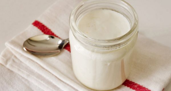 Glas mit Joghurt steht auf einer Serviette, daneben liegt ein Löffel
