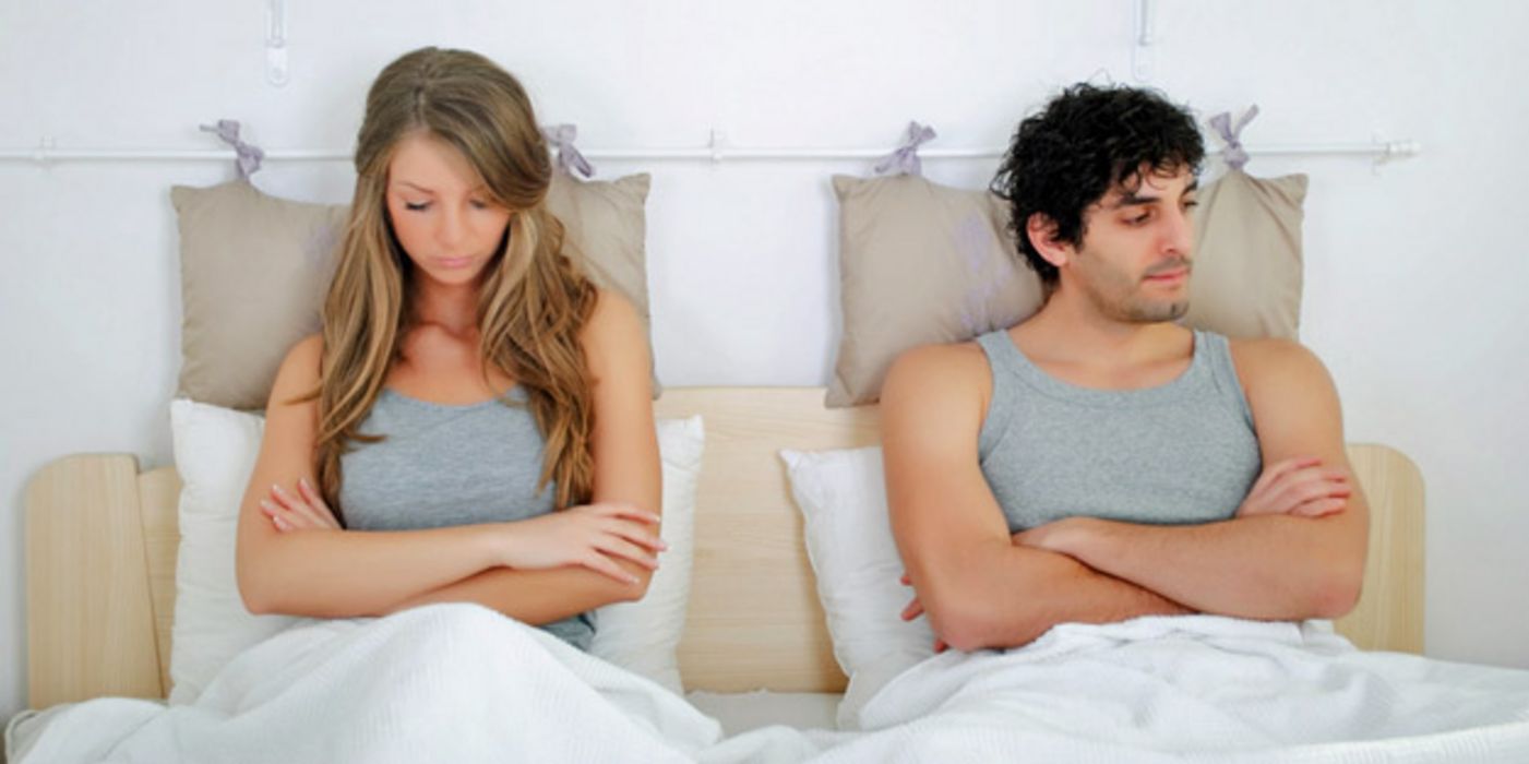 Mann und Frau, sitzen nebeneinander aufrecht im Bett und sind sichtlich frustriert.