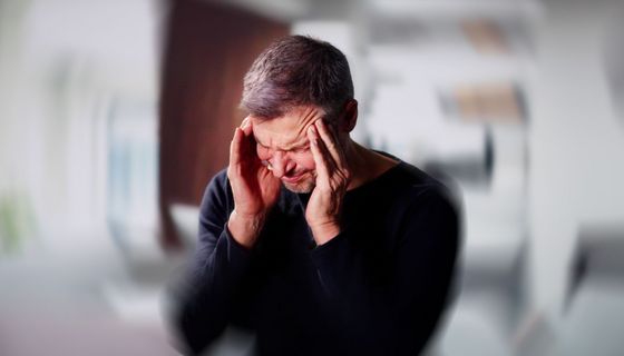 Ein Mann fasst sich an die Schläfe, das Bild um seinen Kopf herum ist kreisförmig verschwommen.