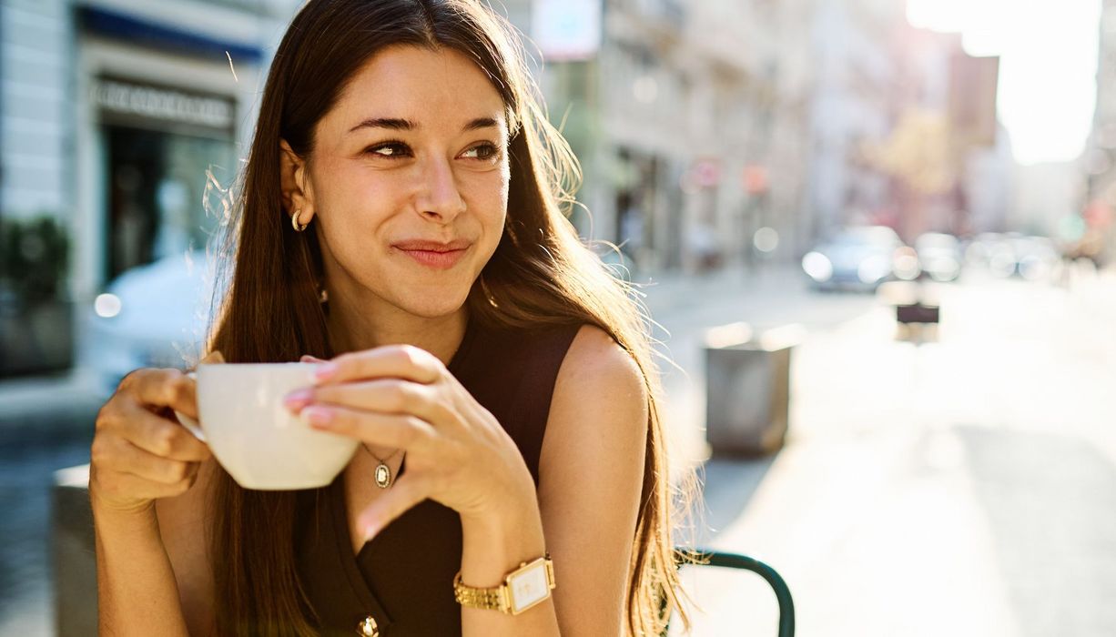 Junge Frau trinkt draußen Kaffee.