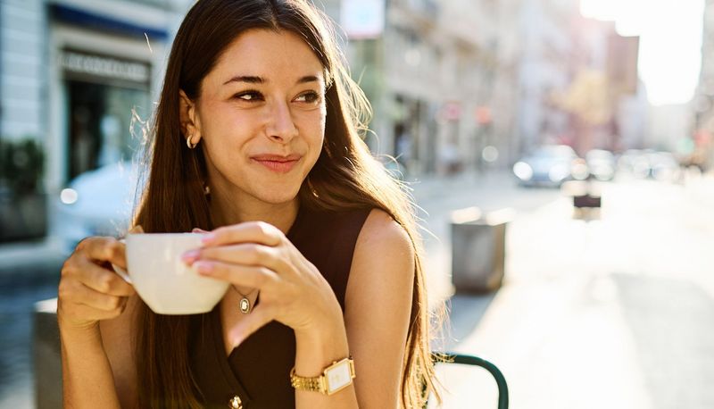 Junge Frau trinkt draußen Kaffee.