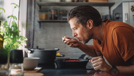 Mann probiert Mahlzeit mit großem Löffel direkt aus dem Topf.