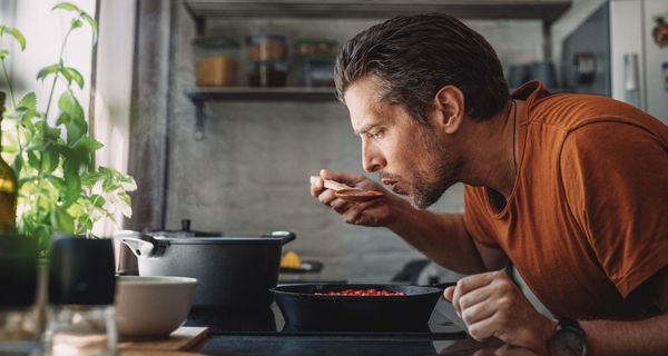 Mann probiert Mahlzeit mit großem Löffel direkt aus dem Topf.