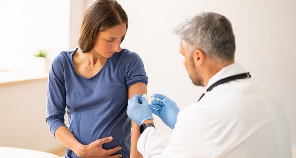 Ein Arzt impft vorsichtig eine Schwangere.