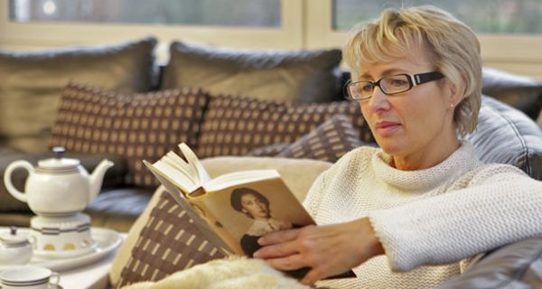 Frau liest Zeitung auf dem Sofa.