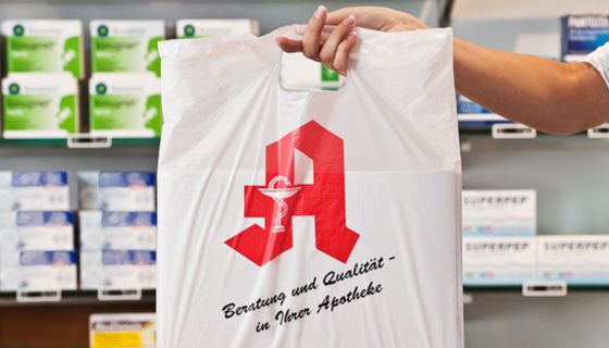 Hand mit Apothekentüte vor Apothekenregalen