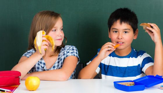 Schülerin und Schüler sitzen im Klassenraum und essen ihr Frühstück
