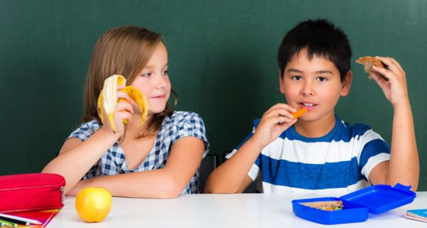 Schülerin und Schüler sitzen im Klassenraum und essen ihr Frühstück 