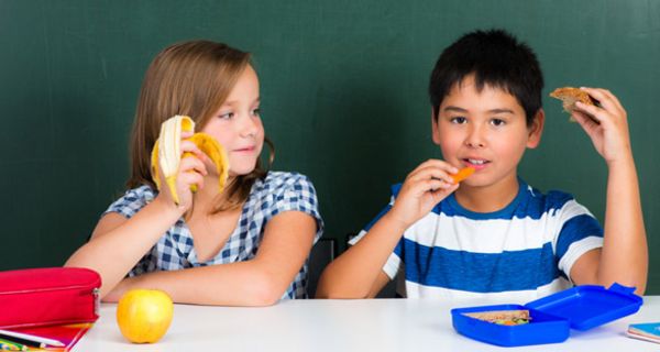 Schülerin und Schüler sitzen im Klassenraum und essen ihr Frühstück
