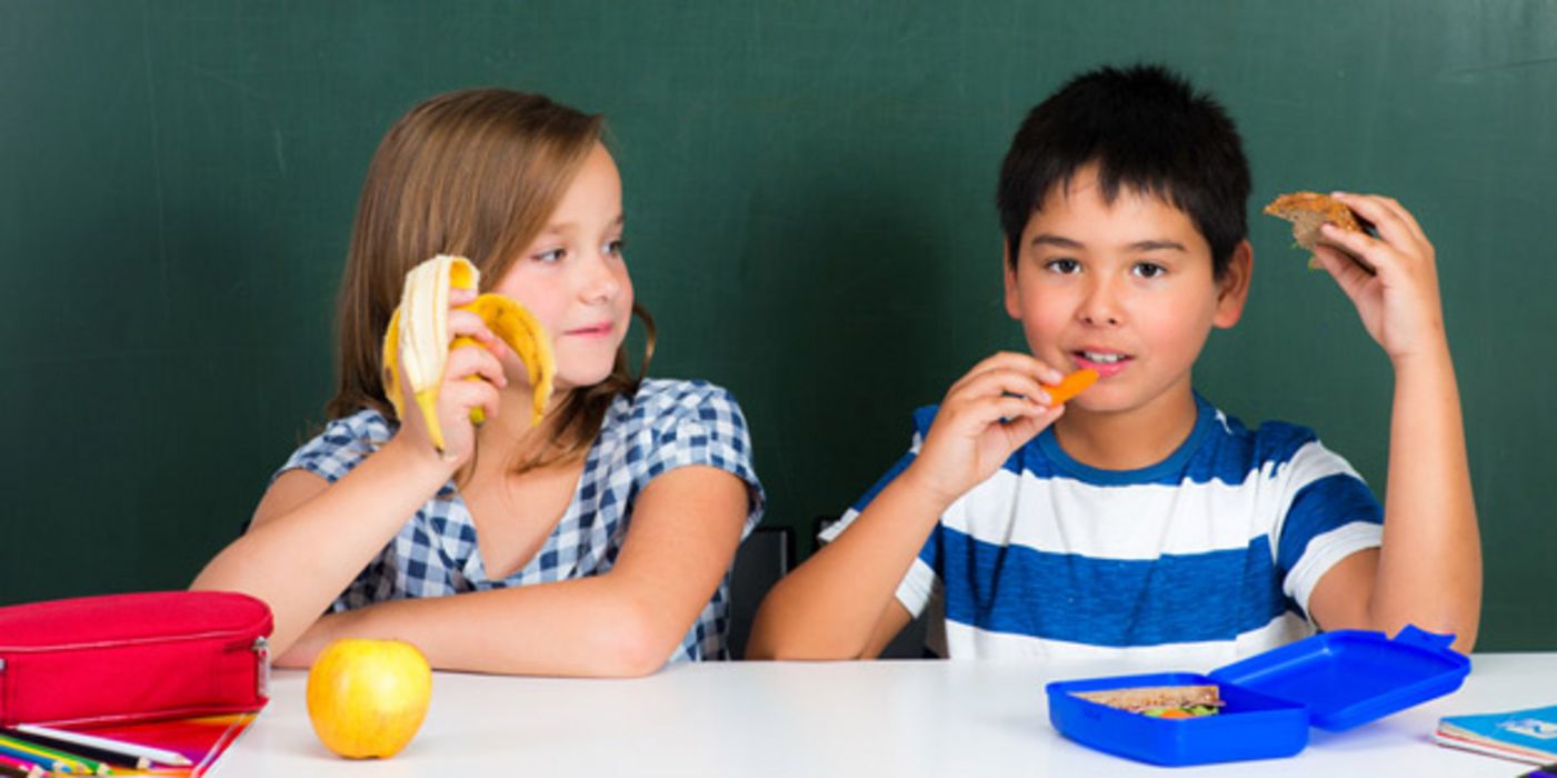 Schülerin und Schüler sitzen im Klassenraum und essen ihr Frühstück 