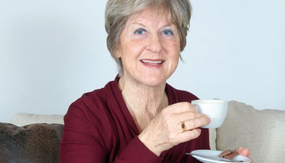 Ältere Frau in dunkelroter Bluse mit Kaffeetasse in der Hand
