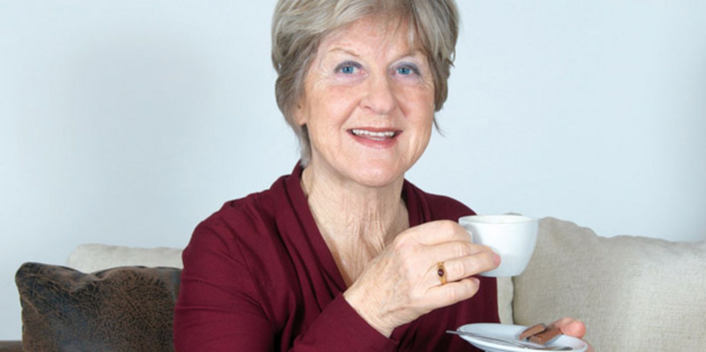 Ältere Frau in dunkelroter Bluse mit Kaffeetasse in der Hand