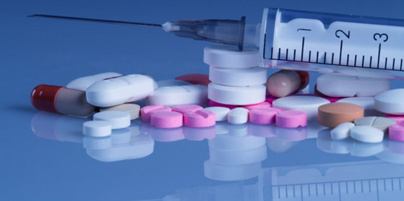 Spritze und verschiedene Tabletten vor blauem Hintergrund