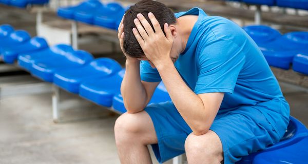 Mann, sitzt in einem Sportstadion und hält sich den Kopf.