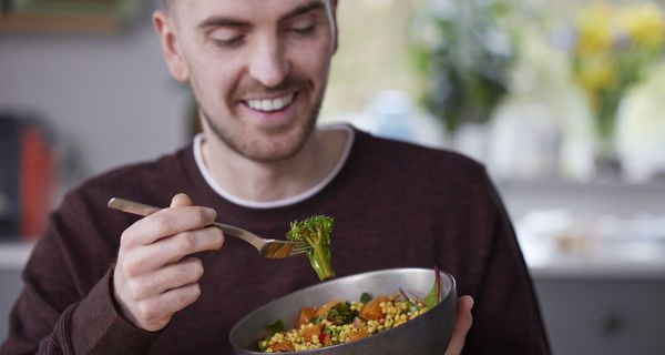 Mann isst ein veganes Gericht mit Samen, Brokkoli und Tomaten.
