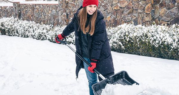 Eine junge Frau schippt gutgelaunt Schnee.