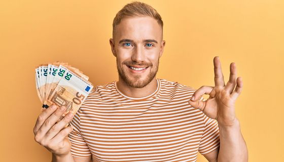 Mann hält lächelnd 50-Euro-Scheine in der Hand.