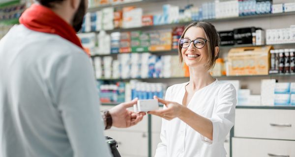 Junge Apothekerin, reicht ein Medikament über die Theke.