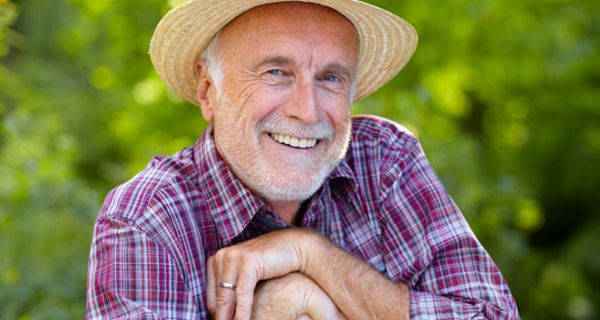 Fröhlicher, älterer Mann im Garten lächelt in die Kamera