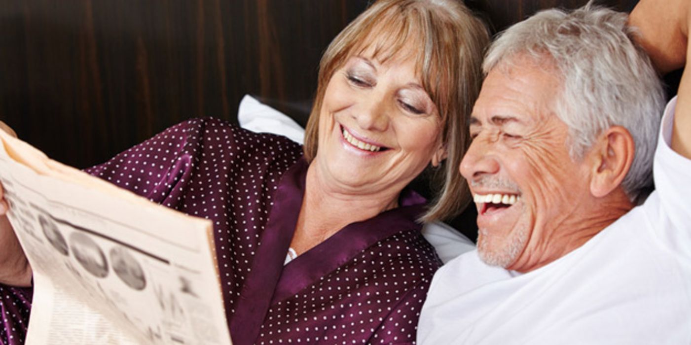 Gut gelauntes, vitales, älteres Paar liest lachend eine Zeitung