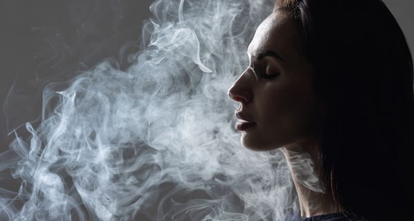 Junge Frau im seitlichen Profil mit Rauchschwaden um den Kopf