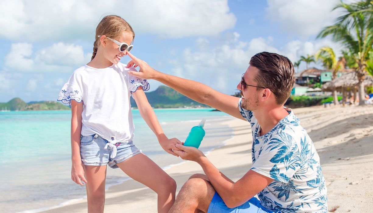 Vater und Tochter am Strand, er schmiert ihr Sonnencreme auf die Nase.
