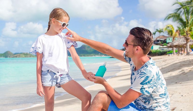 Vater und Tochter am Strand, er schmiert ihr Sonnencreme auf die Nase.