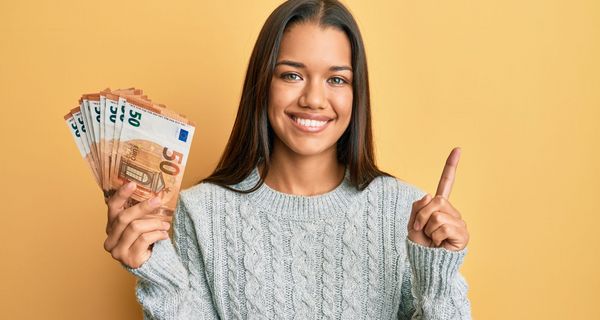 Strahlende Frau im Pullover hält ein Bündel 50-Euro-Scheine in der Hand.