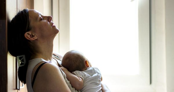 Mutter mit Baby im Arm, lehnt gestresst an der Wand.