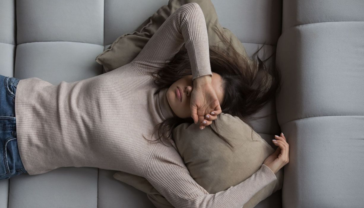 Frau, hält ihre Arme über den Kopf und liegt auf der Couch.