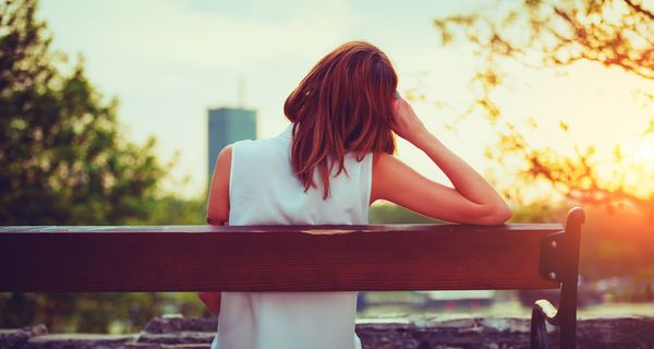 Junge Frau, sitzt allein auf einer Bank.