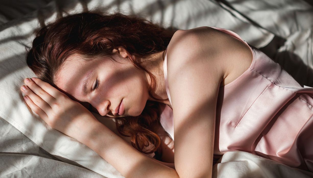 Junges Mädchen liegt im Bett, die Augen leicht geöffnet.