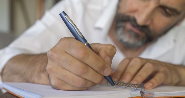 Ein älterer Herr schreibt etwas in ein Notizbuch.