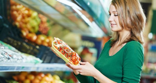 Junge Frau steht vor Supermarkt-Gemüseregal und hält eine Packung Tomaten in den Händen