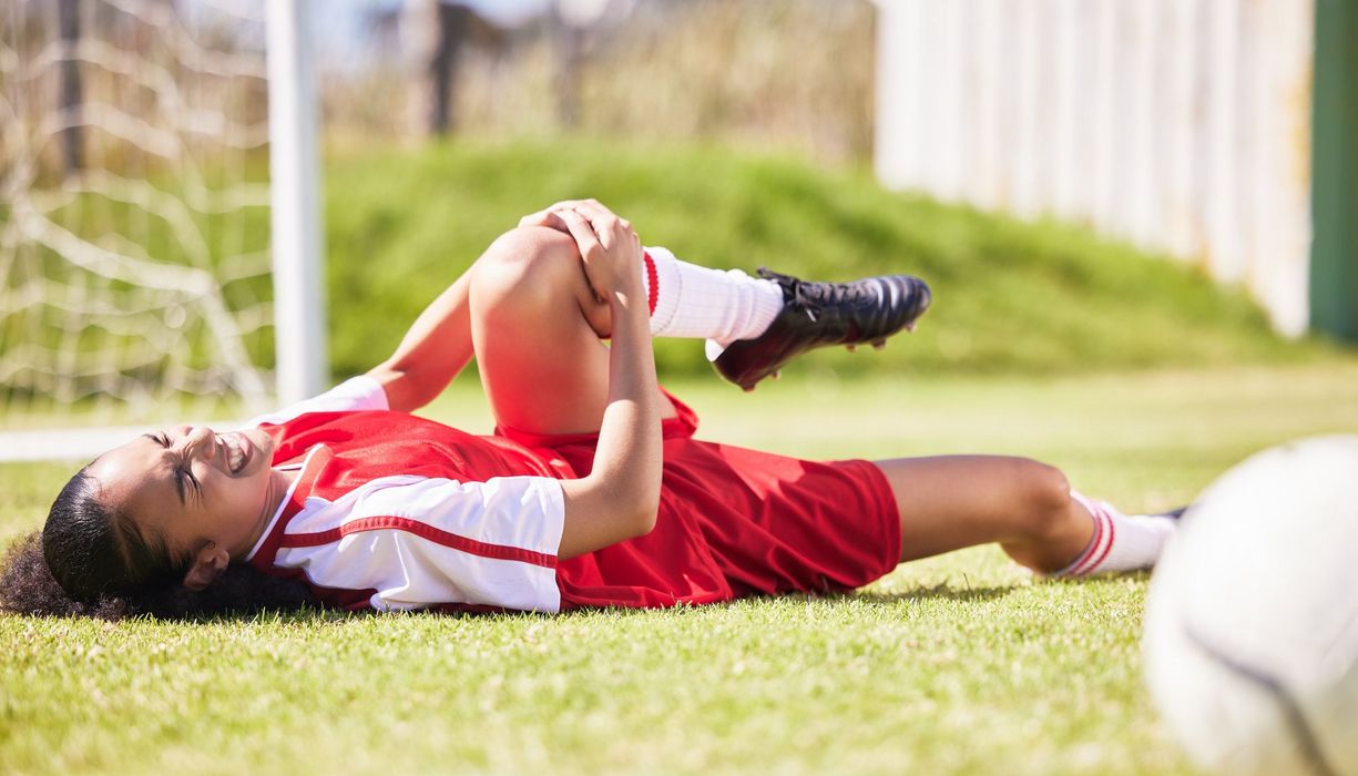 Junge Fußballerin hält sich auf dem Rasen das Knie.
