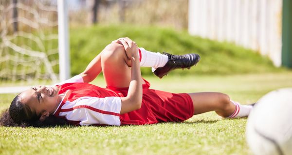Junge Fußballerin hält sich auf dem Rasen das Knie.
