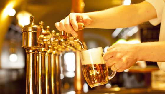 Bierzapfanlage in Kneipe/Pub, Arm von rechts ins Bild ragend zapft gerade ein Bier in einen Humpen.