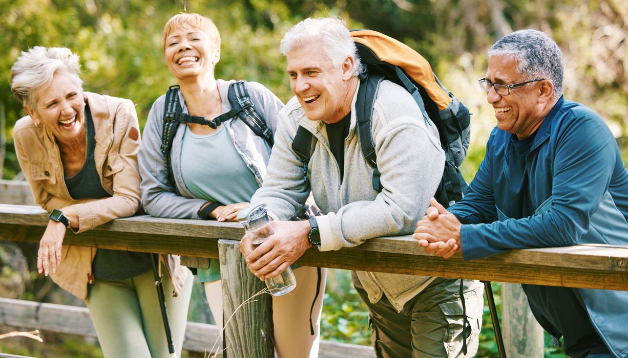 Ältere Menschen machen Rast beim Wandern an einer Brücke und lachen