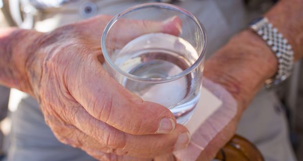 Älterer Mensch, hält ein Glas Wasser.