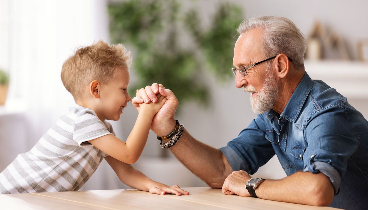 Älterer Mann macht Armdrücken mit seinem Enkel.