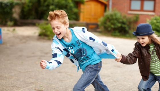 Junge und Mädchen rennen Hand in Hand über den Pausenhof.