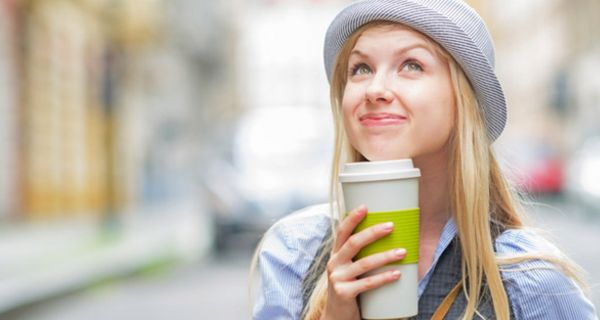 Junge Frau mit Hut trinkt Kaffee im Freien.