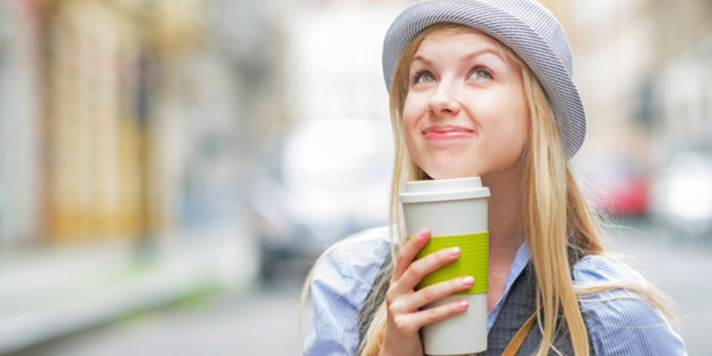 Junge Frau mit Hut trinkt Kaffee im Freien.