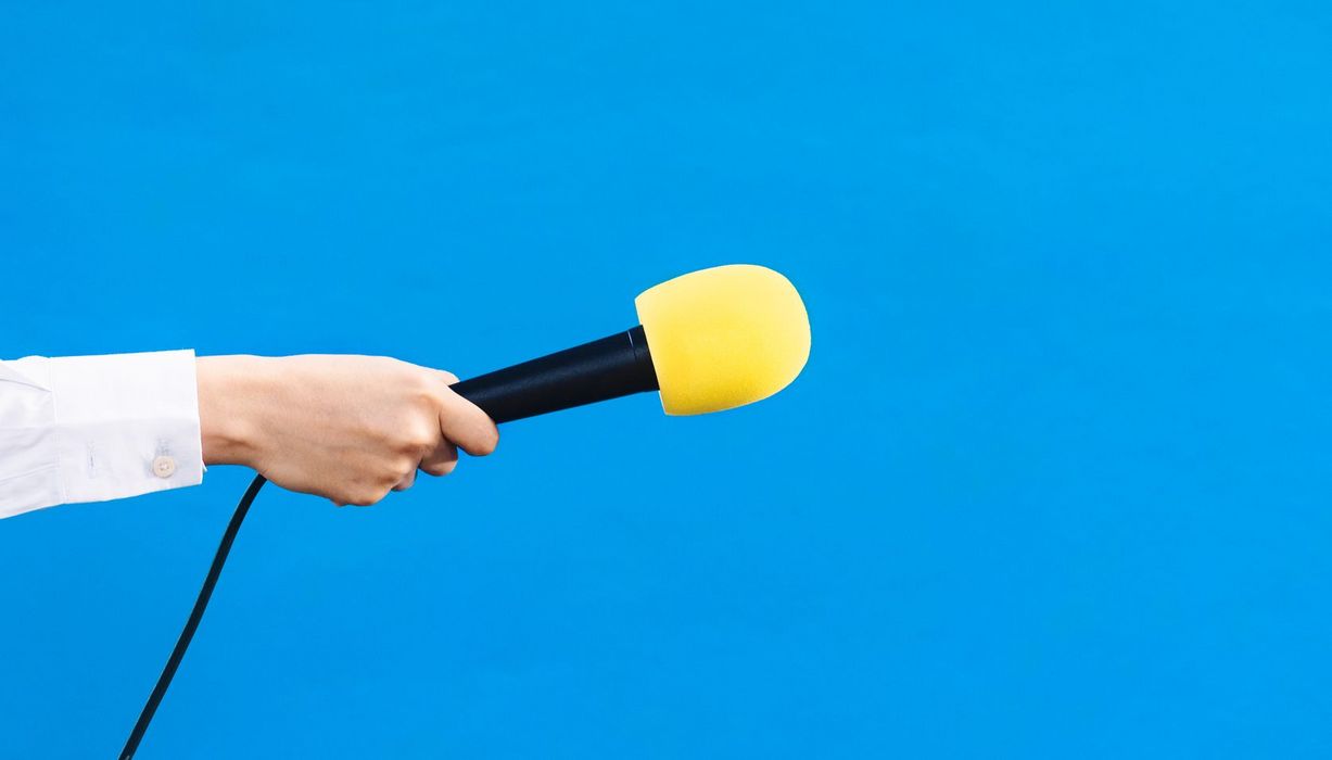 Hand hält gelbes Mikrophon vor blauem Hintergrund.