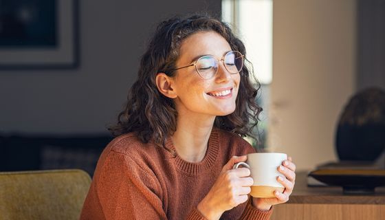 Junge Frau mit Brille trinkt eine Tasse Kaffee.