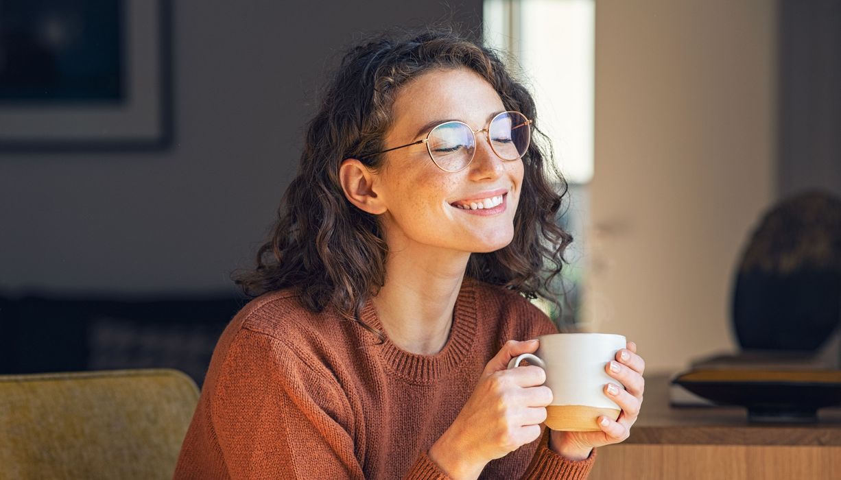 Junge Frau mit Brille trinkt eine Tasse Kaffee.
