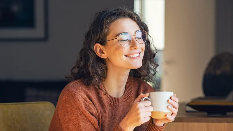 Junge Frau mit Brille trinkt eine Tasse Kaffee.