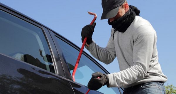 Mann mit Maske hebelt Autotür auf